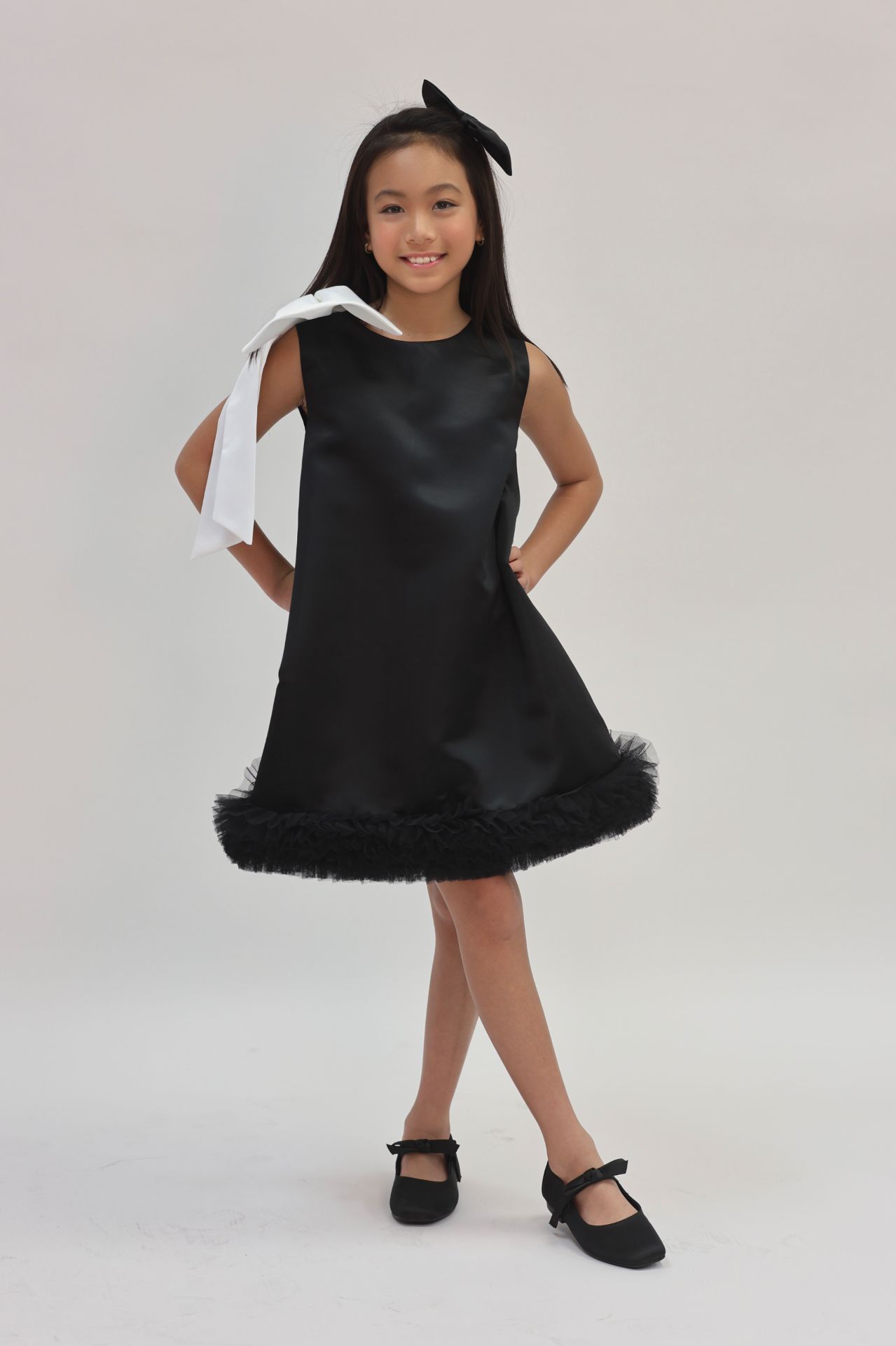 Editorial studio portrait in black satin shift dress with white bow and tulle hem