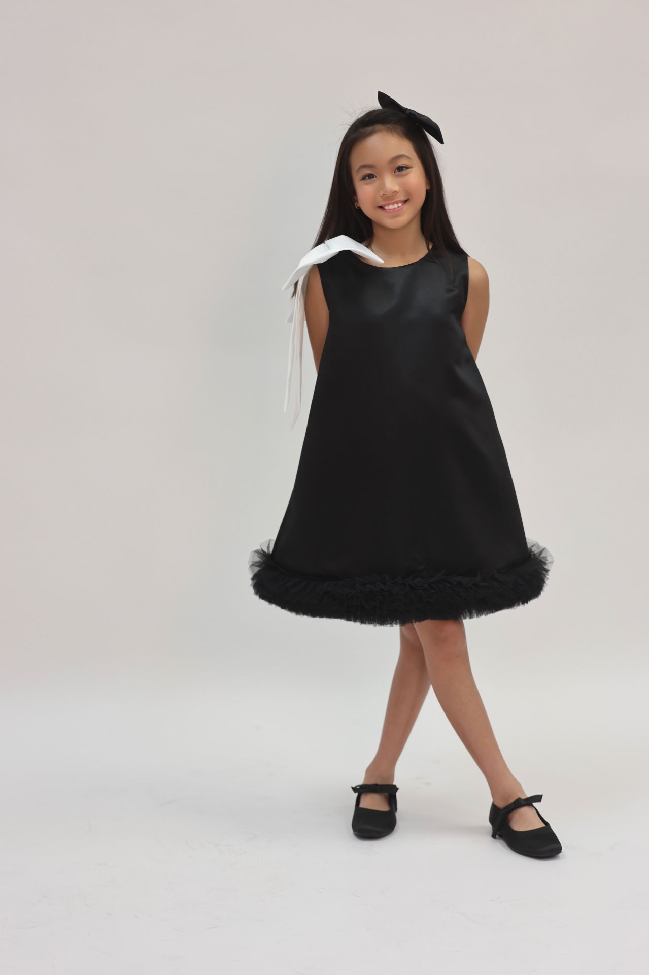 Full-length studio editorial in black satin shift dress with tulle hem