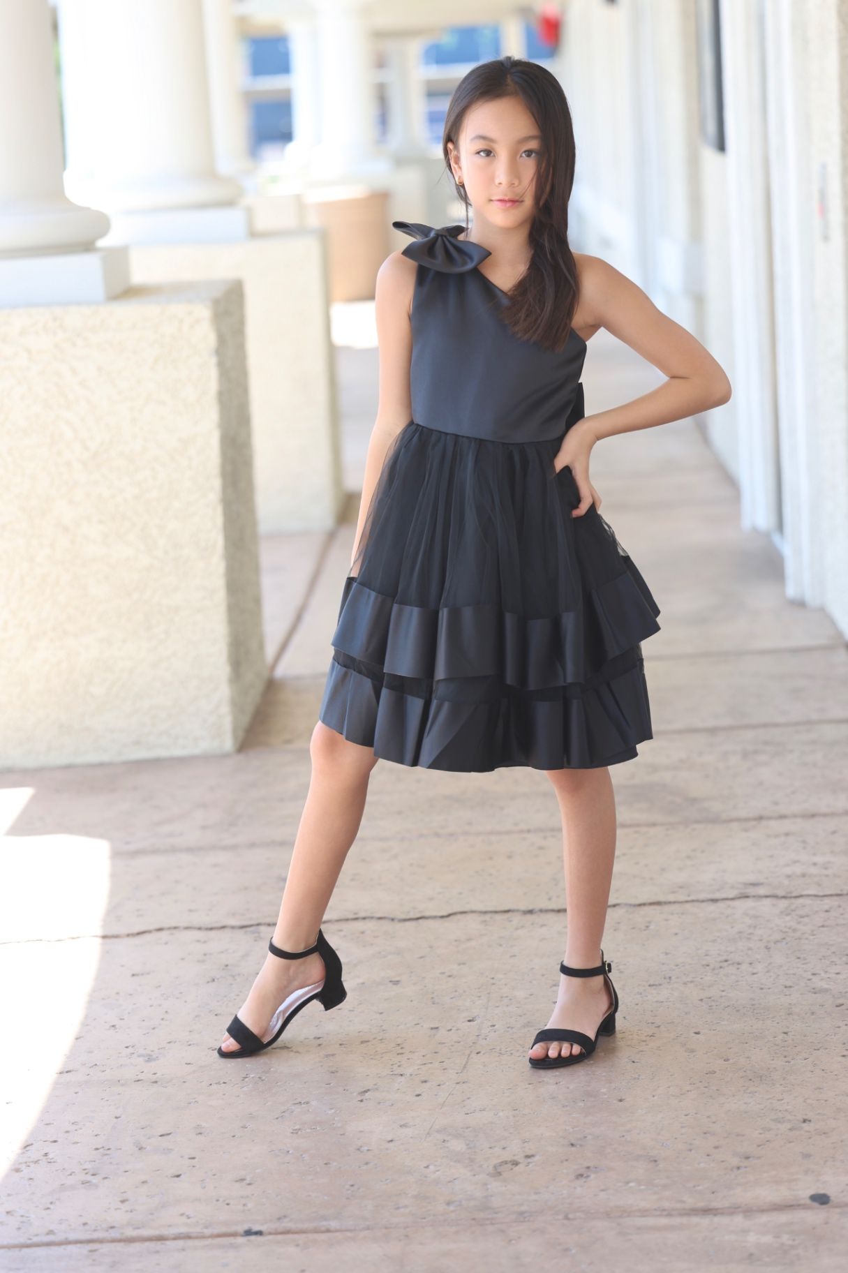 Outdoor editorial in black one-shoulder tiered dress, confident stance