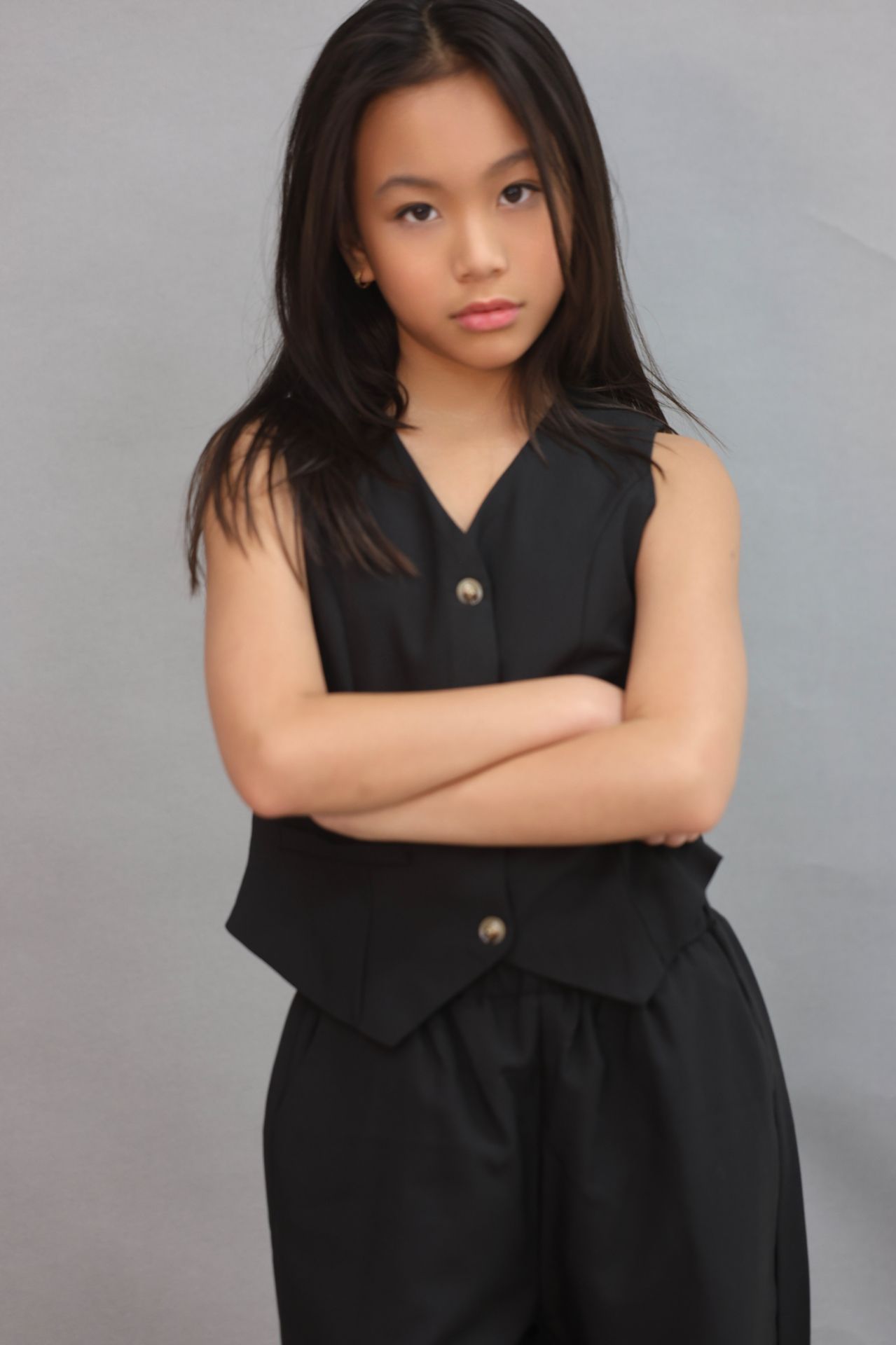 Editorial portrait in black tailored vest and trousers, arms crossed